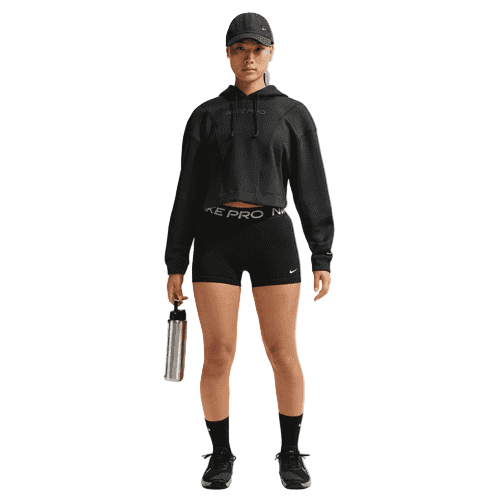 En kvinde i sort Nike træningstøj, herunder en cropped hoodie, Mid-Rise 3 Biker Shorts Dame Black/White, sokker, sneakers og en kasket holder en sølvfarvet vandflaske. Tøjet har synlig Nike-branding på en almindelig hvid baggrund.