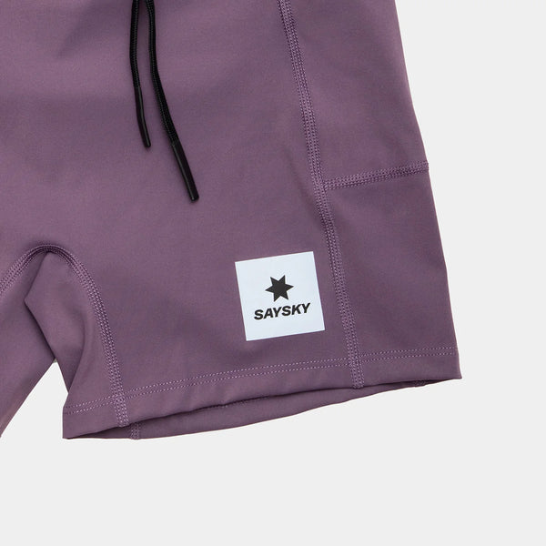 Nærbillede af den nederste del af Saysky W Flow+ Race Short Tights 4" i lilla, med sorte snore og et hvidt rektangulært mærke med en sort stjerne og "SAYSKY" nær kanten.