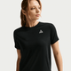 En kvinde med lysebrunt hår i hestehale bærer Nike ACG Short-Sleeve Running Top til kvinder, sort/summit white, med et lille hvidt trekantlogo på brystet - perfekt til trailløb og vist på en neutral baggrund.