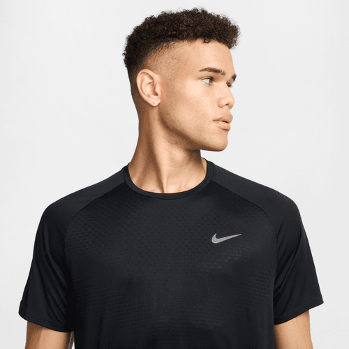 En ung mand med kort krøllet hår, iført den sorte Nike Stride SS løbetop til mænd med reflekterende sølvdetaljer og Dri-FIT ADV-teknologi, kigger til venstre for sig på en almindelig lys baggrund.