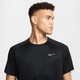 En ung mand med kort krøllet hår, iført den sorte Nike Stride SS løbetop til mænd med reflekterende sølvdetaljer og Dri-FIT ADV-teknologi, kigger til venstre for sig på en almindelig lys baggrund.