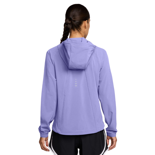 Der ses et billede bagfra af en person med flettet hår, der bærer Nike Swift Repel Packable løbejakken til kvinder i farvekombinationen Purple Pulse/Reflective Silver samt sorte shorts med hvid kant. Jakken, der er designet til en aktiv livsstil, har fire små vandrette striber på ryggen.