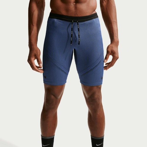 En person er iført blå Nike Dfadv Aroswft Bf Htight løbetights (Herre, Game Royal/Diffused Blue/Obsidian/Black) med blå ribbede shorts og sorte Nike-sokker. Billedet er beskåret fra midt på torsoen til lige under knæene.