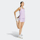 En kvinde i en Adidas Adizero E Tank, Dame, Powplu, med hvide sneakers, står på et ben og strækker låret mod en almindelig baggrund - perfekt løbetøj i hurtigtørrende materiale.