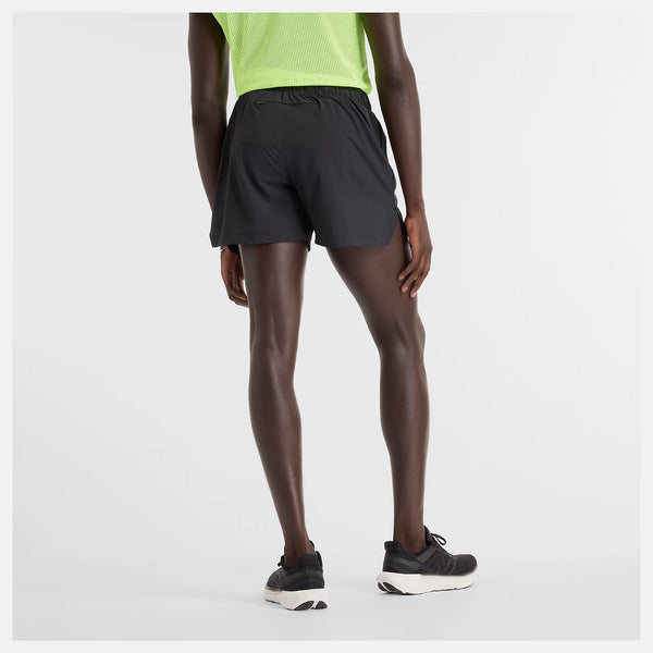 En person står med front mod kameraet iført en neongrøn trøje, New Balance RC Short 5", Herre, sorte shorts, sorte sokker og sorte løbesko på en almindelig hvid baggrund.