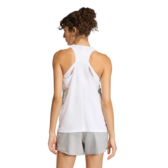 En kvinde med krøllet hår bærer Adidas Adi365 Running Iconic Tank Top i hvid med racerback og åndbart stof sammen med lysegrå shorts på en ensfarvet lys baggrund.