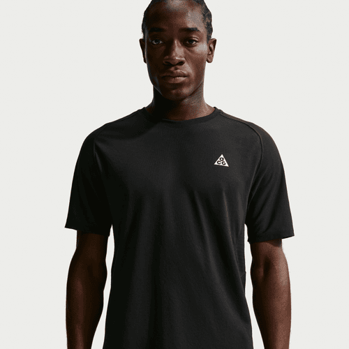 En mand står på en lys baggrund iført Nike ACG "Solar Chase" Trail Running Top til mænd i Black/Black/Summit White med et lille hvidt trekantet logo på venstre bryst.