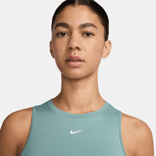 En kvinde med mørkt hår, der er trukket tilbage, bærer en Nike Dri-FIT Classic Tank Top i Cannon/White og ser direkte ind i kameraet mod en almindelig lys baggrund.