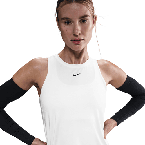 En kvinde iført Nike Dri-FIT Classic Tank Top til kvinder i hvid/sort med sorte ærmer står med hænderne på hofterne mod en hvid baggrund.