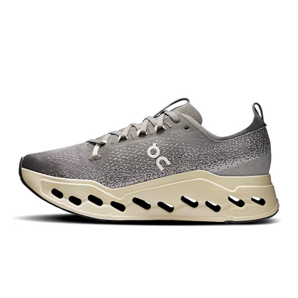 On Cloudsurfer Max, Herre i Asphalt/Ice har en overdel i mesh, lysegrå snørebånd, en tyk beige sål med ovale udskæringer, trækflig i hælen og et lille hvidt logo - en kombination af maksimal komfort og design inspireret af den originale Cloudsurfer Max.