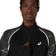 En person iført Limited Series Lite-Show Ls Top fra Asics i Performance Black med hvide refleksdetaljer og ASICS-logo holder lynlåsen i midten. Baggrunden er ensfarvet hvid.