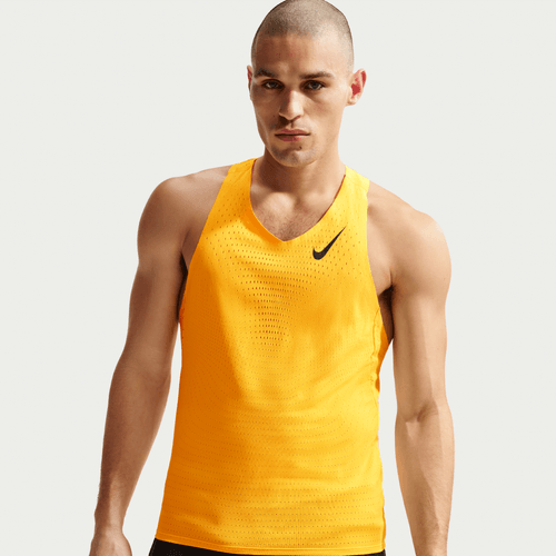 En mand iført Nike AeroSwift Running Singlet, Herre, i Laser Orange/Black står på en almindelig lys baggrund og ser lige frem med et neutralt udtryk.