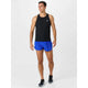 En mand står på en almindelig hvid baggrund iført en sort New Balance Race Day Ultra Light Singlet, lyseblå løbeshorts og sorte løbesko. Han kigger til siden og smiler, klar til Race Day.