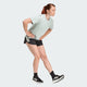 En kvinde i sportstøj bøjer sig frem for at strække sine haser iført en lys t-shirt, sorte Adidas Adi365 Shorts, Dame og sorte sneakers - de perfekte lette shorts til aktive kvinder.
