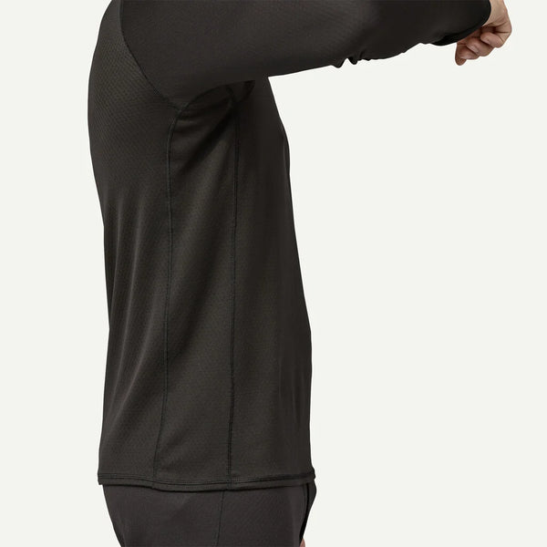 En mand er iført en sort Patagonia Cap MW Crew, Herre, set fra siden med højre arm bøjet og løftet. Kun hans overkrop og overben er synlige mod en almindelig lys baggrund.