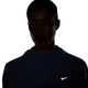 En person iført en mørk lilla Nike Swift Repel Packable løbejakke til kvinder med et synligt, reflekterende sølvfarvet Nike-logo står foran en hvid baggrund; personens ansigt er stort set i skygge.