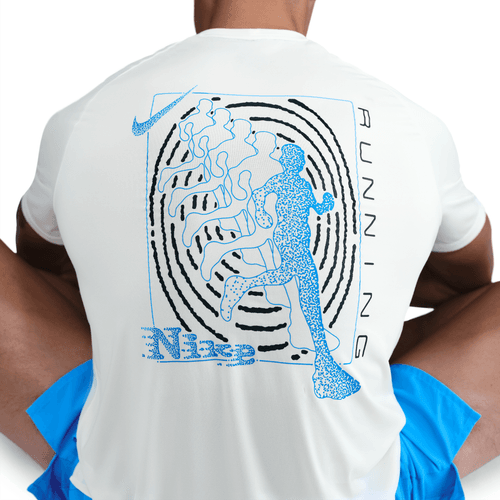 En person sidder med benene over kors, set bagfra, iført en hvid Nike Stride Running Short-Sleeve Top (Herre, Sail) med en blå og sort abstrakt løbegrafik og "Nike" med "RUNNING" trykt lodret på ryggen.