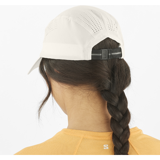 En person med mørk fletning bærer en Salomon SHKOUT Cap U i Whisper White med ventilationshuller og justerbar pasform sammen med en gul top. Billedet er taget bagfra.
