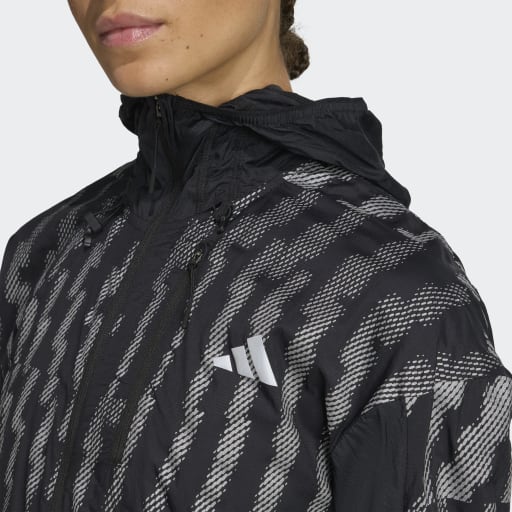 En person iført Adidas Adi365 Jacket til kvinder i Black/Refsil med hvide striber og et Adidas-logo på brystet, vist fra skuldrene og op med en del af ansigtet synligt.