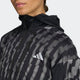 En person iført Adidas Adi365 Jacket til kvinder i Black/Refsil med hvide striber og et Adidas-logo på brystet, vist fra skuldrene og op med en del af ansigtet synligt.