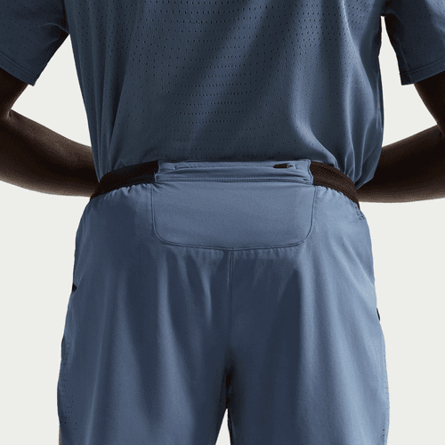 En person iført en blå perforeret skjorte og Nike AeroSwift 4In Brief-Lined Running Shorts til mænd i Diffused Blue/Black med en lynlåslomme på bagsiden af linningen ses bagfra og fra taljen og op.