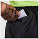 En persons hånd placerer et rektangulært hvidt kort i lynlåslommen på New Balance RC Short 5", Herre, Black, mens han er iført en lysegrøn perforeret top.