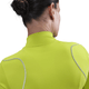 En kvinde med mørkt hår i en knold bærer Nike Therma-FIT ADV 1/2-Zip Reflective Running Top til kvinder i Cyber/Reflective Silver, set bagfra mod en ensfarvet baggrund.