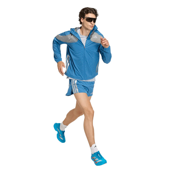 En person i blå jakke, Adidas Adizero Hakone Ekiden Shorts Herre Duinn, blå løbesko og solbriller jogger mod en almindelig hvid baggrund.