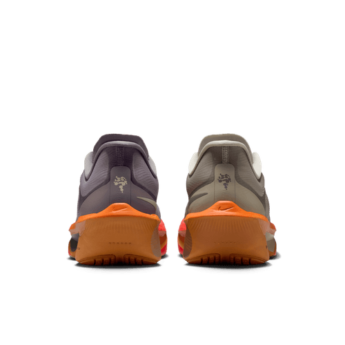 To Nike-sneakers, bl.a. Zoom Fly 6 herre i Desert Khaki/Cave Stone-Monarch, er vist bagfra på en lys baggrund. Den venstre er lilla/grå med en orange sål; den højre er olivengrøn/grå - ideel til tempoløb.