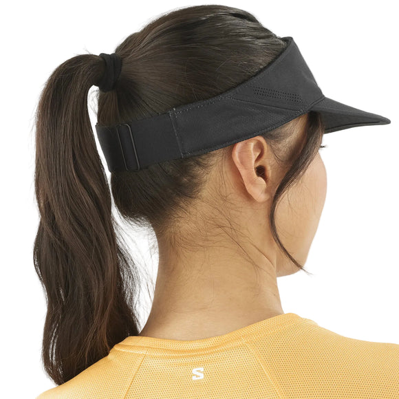 En person med langt brunt hår i hestehale bærer en gul sportstrøje og Salomon SHAKEout Visor, Unisex, Black, set bagfra. Det justerbare design giver komfort og pasform til enhver aktivitet.