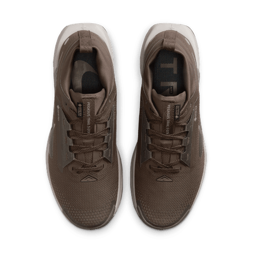 Et par Nike Pegasus Trail 5 Gore-Tex Dame-sko i Ironstone/College Grey-Velvet Brown vises ovenfra på en hvid baggrund; disse vandtætte løbesko har snørebånd og synlig tekst langs tungen.
