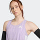 En lyshåret kvinde med rødt hår er iført Adidas Adizero Singlet, Dame, Powplu/Maglil med sorte ærmer og poserer med den ene arm bøjet. Den svedtransporterende top står i kontrast til den ensfarvede, lyse baggrund.