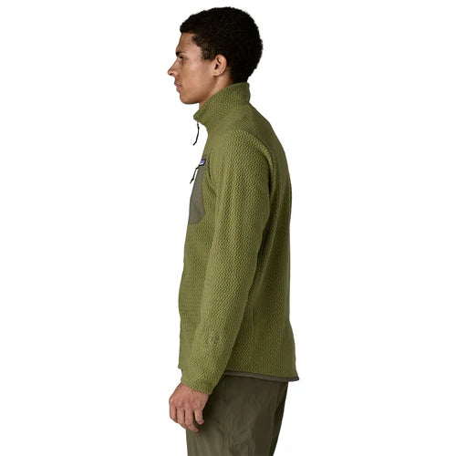 En mand står i profil mod venstre iført en Patagonia R1 Air Jacket, Herre, i Caper Green med matchende grønne bukser på en almindelig hvid baggrund.