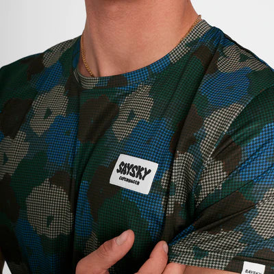 Nærbillede af en person iført Saysky Flower Combat T-Shirt, Herre, Blue Aop. Den nederste halvdel af ansigtet og overkroppen er vist, og brystmærket er fremhævet.