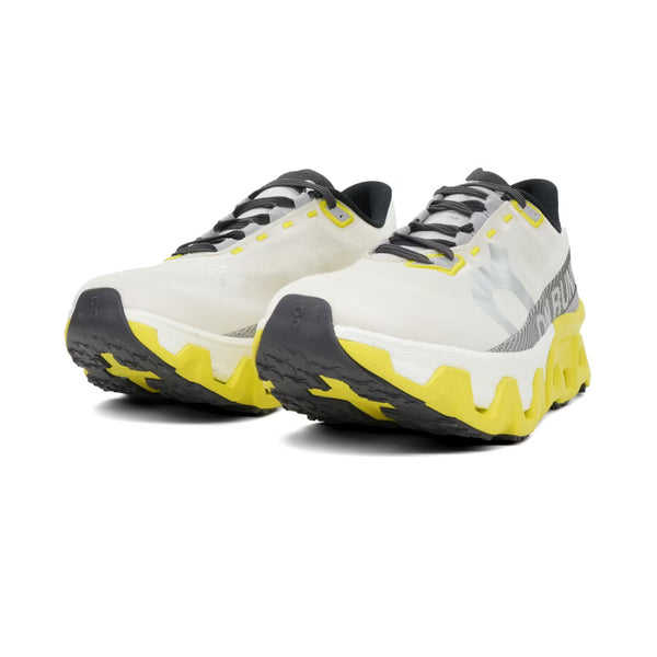 Et par On Cloudmonster Hyper dame løbesko i Dew/Lime med hvid overdel, sorte snørebånd og detaljer samt chunky gule og sorte såler, her set forfra fra en vinkel.