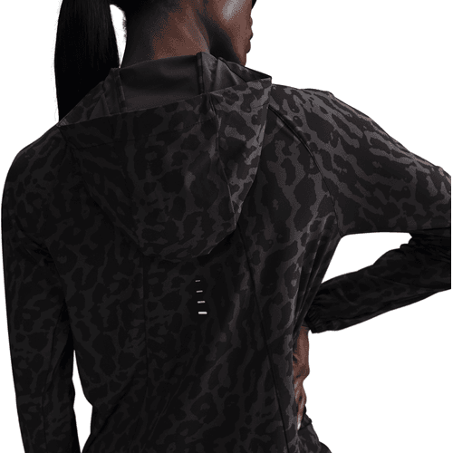 En person iført en Nike Dri-FIT løbejakke til kvinder i Black/Anthracite/Reflective Silver står med den ene hånd på hoften og kigger væk fra kameraet mod en hvid baggrund.