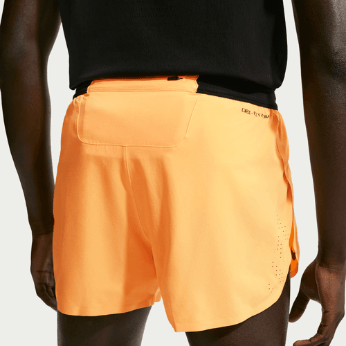 En person set bagfra er iført lyse laserorange/sorte Nike AeroSwift 4In Brief-Lined Running Shorts, Herre, med linningen og den lille baglomme tydeligt synlige.