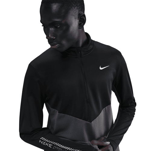 En person i Nike Pacer Winterized 1/2-Zip Running Top (Herre, Anthracite/Black/Reflective Silv) står på en hvid baggrund og kigger ned og til siden med en hånd i nærheden af taljen.