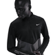 En person i Nike Pacer Winterized 1/2-Zip Running Top (Herre, Anthracite/Black/Reflective Silv) står på en hvid baggrund og kigger ned og til siden med en hånd i nærheden af taljen.