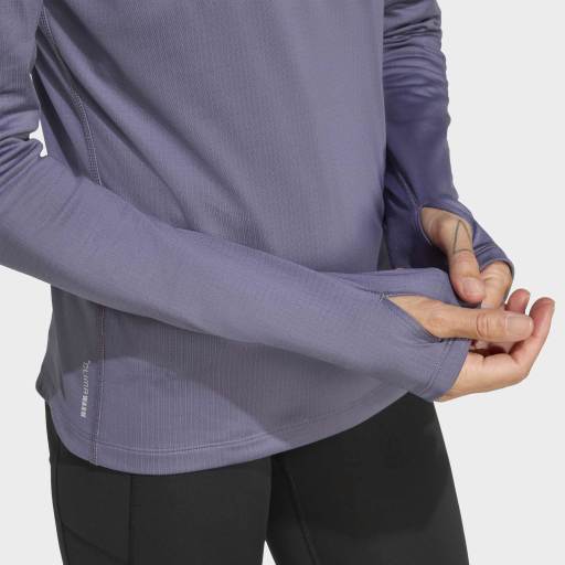 En kvinde justerer ærmet på en langærmet, lyslilla Adidas Otr Bin Hz, Dame, Previo træningstrøje med AEROREADY og tommelfingerhuller. Kun hendes overkrop og arme er synlige, parret med sorte bukser - ideel løbetøj til damer.