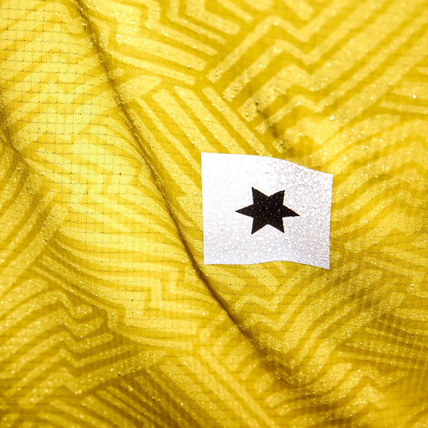 Et nærbillede af Saysky Reactive Flow Singlet, Herre, Yellow Aop viser det geometriske zigzagmønster og en lille hvid firkant med en sort stjerne, der fremhæver åndbart træningstøj-designet.