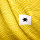 Et nærbillede af Saysky Reactive Flow Singlet, Herre, Yellow Aop viser det geometriske zigzagmønster og en lille hvid firkant med en sort stjerne, der fremhæver åndbart træningstøj-designet.