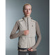 En kvinde iført On Weather Vest, Dame in Desert/Eclipse over en taupe langærmet skjorte står med front mod en grå baggrund og lyner den ærmeløse, lysbeige vest op med den ene hånd.