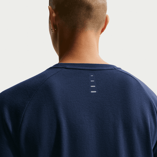 En person med kort hår og en ørering ses bagfra iført en Nike Stride Waffle Crew løbetrøje til mænd i Midnight Navy/Reflective Silver med fire små vandrette hvide linjer under halsudskæringen.
