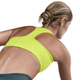 En kvinde med blondt hår i en lav knold ses bagfra iført Nike Swoosh Medium Sports Bra, Dame, i Cyber/White, sammen med mørke sportsbukser på en almindelig hvid baggrund.
