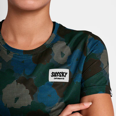 En person iført Saysky W Flower Combat T-Shirt, Dame, Blue Aop med SAYSKY COPENHAGEN-mærke på brystet. Kun underansigtet, halsen og overkroppen er synlige.