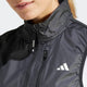 Nærbillede af en kvinde iført den sorte Adidas Otr B Vest med høj krave og hvidt logo på brystet. Vesten er en del af den seneste dame løbetøj-kollektion og viser hendes ansigt i et delvist billede, hvor hun smiler lidt.