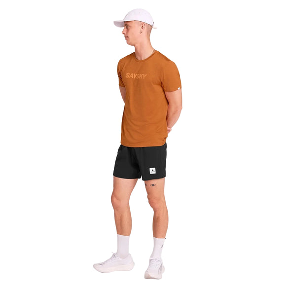 En mand iført Saysky Logo Pace T-Shirt til mænd i orange, sammen med shorts og en hat.