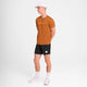En mand iført Saysky Logo Pace T-Shirt til mænd i orange, sammen med shorts og en hat.