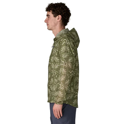 En mand med kort, krøllet hår står i profil iført Patagonias Houdini-jakke til mænd i Sand Waves/Caper Green og mørke bukser. Baggrunden er helt hvid.